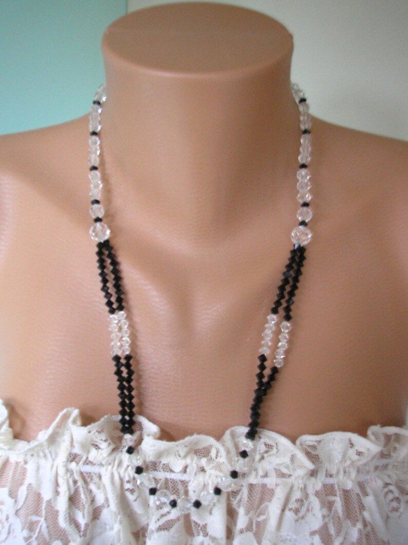 May include: A double strand necklace with alternating black and clear crystal beads. The necklace is displayed on a white lace-covered mannequin bust.