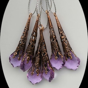 May include: Six purple crystal teardrop pendants with ornate copper filigree accents hanging from silver cords.