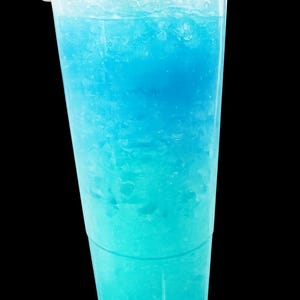 May include: A clear plastic disposable cup filled with a bright blue slushy beverage. The drink features a gradient of color, transitioning from a deeper blue at the top to a lighter, vibrant turquoise shade at the bottom, topped with a clear lid.