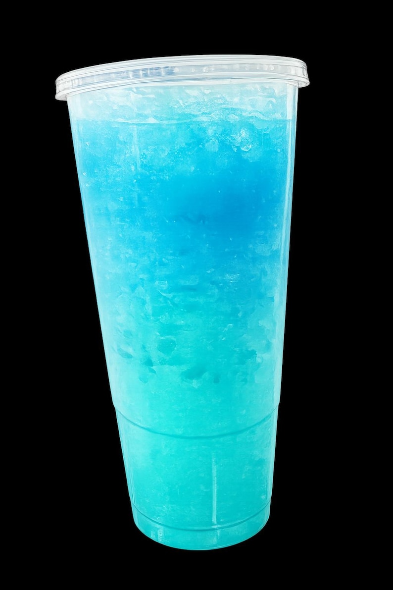 May include: A clear plastic disposable cup filled with a bright blue slushy beverage. The drink features a gradient of color, transitioning from a deeper blue at the top to a lighter, vibrant turquoise shade at the bottom, topped with a clear lid.