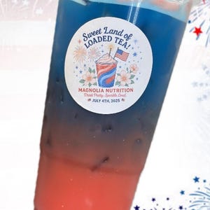 May include: A clear plastic cup filled with a layered red and blue iced beverage. A circular white sticker on the front features the text Sweet Land of LOADED TEA! MAGNOLIA NUTRITION Drink Pretty. Sparkle Loud. JULY 4TH, 2025 with a graphic of a drink.