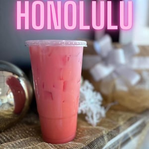 May include: A clear plastic cup filled with a pink iced beverage and ice cubes. The word HONOLULU is displayed in large, glowing pink capital letters above the cup. The drink is served in a tall, tapered container with a flat, transparent lid.