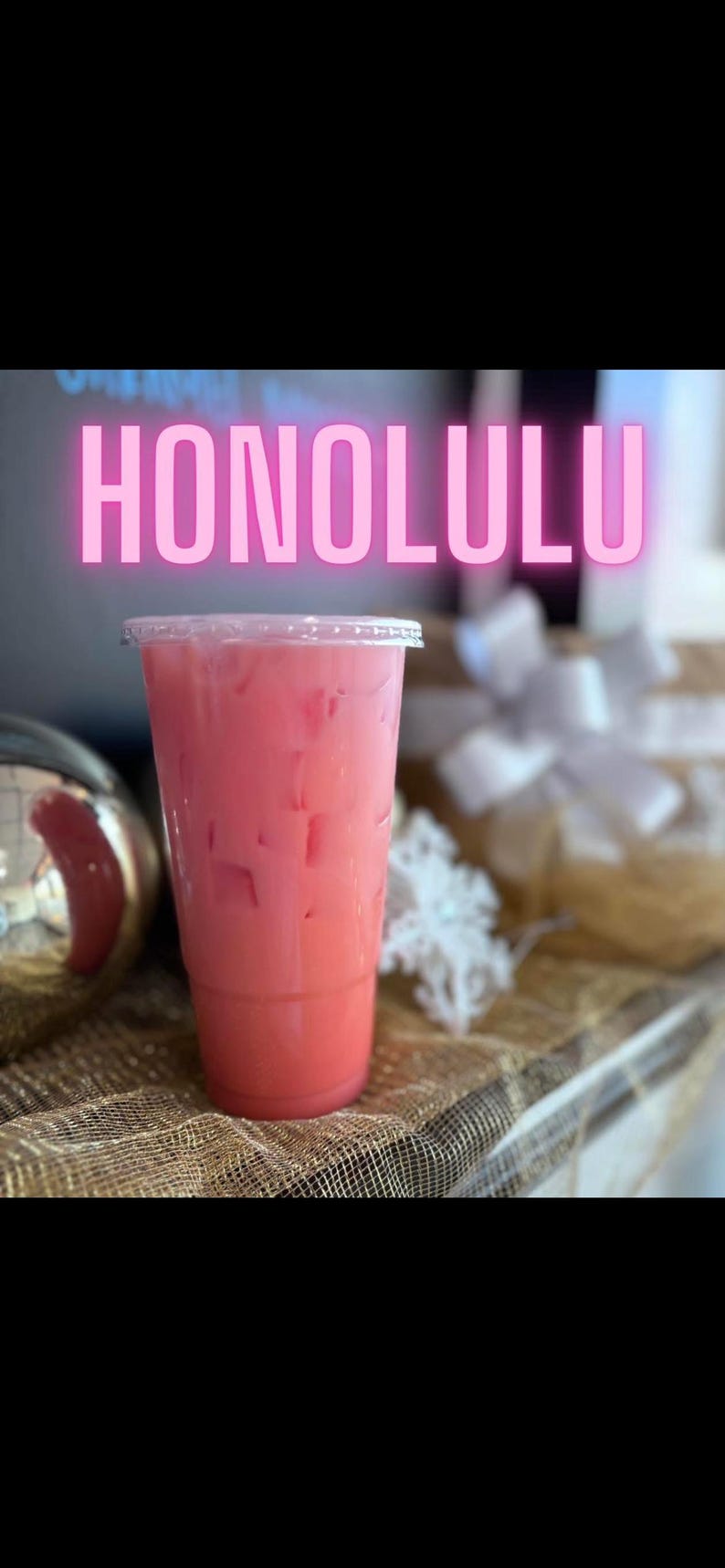 May include: A clear plastic cup filled with a pink iced beverage and ice cubes. The word HONOLULU is displayed in large, glowing pink capital letters above the cup. The drink is served in a tall, tapered container with a flat, transparent lid.