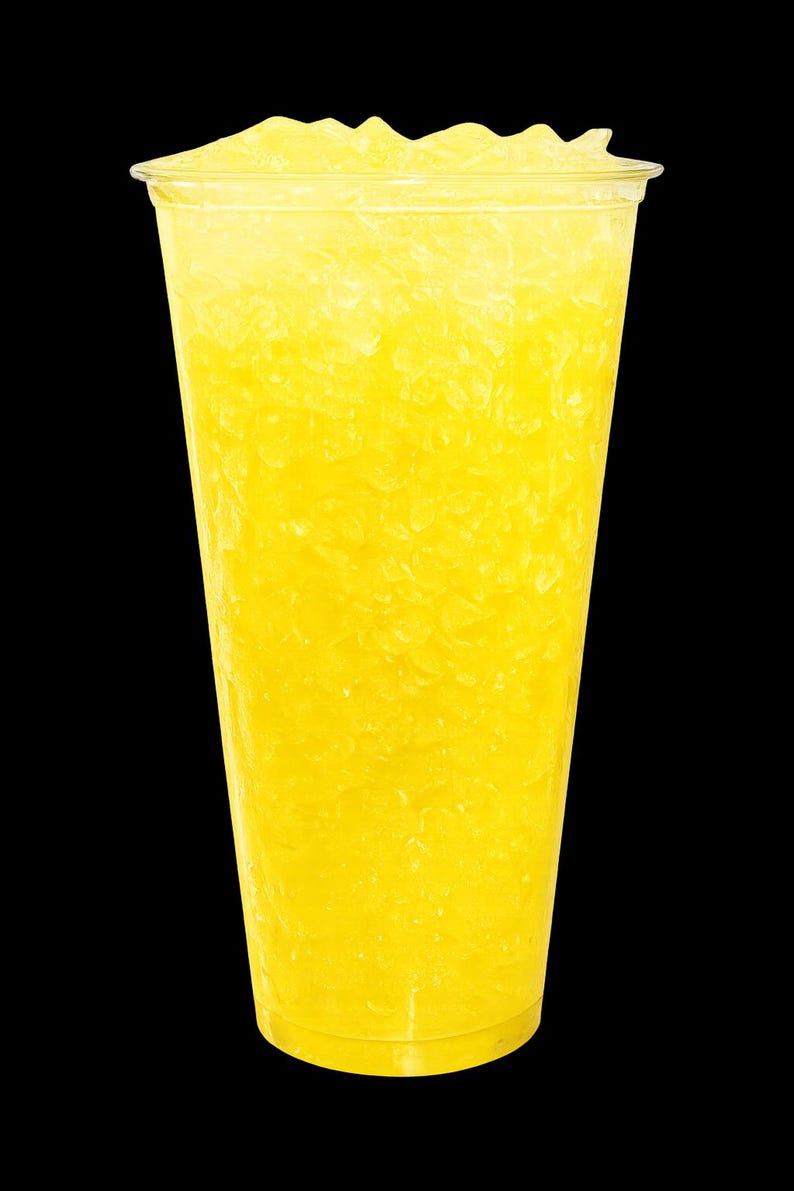 May include: A clear plastic cup filled with a bright yellow, icy beverage. The drink is packed with crushed ice, creating a textured, slushy appearance that fills the container from the bottom to the top rim against a solid black background.