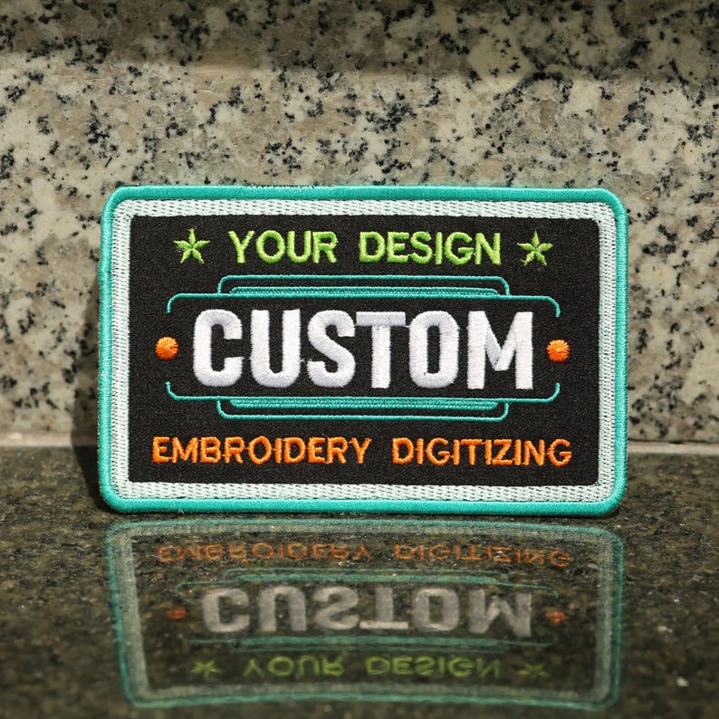 May include: Black embroidered patch with white text that says "CUSTOM" and orange text that says "EMBROIDERY DIGITIZING". The patch has a teal border and a white star with green text that says "YOUR DESIGN" above the word "CUSTOM".
