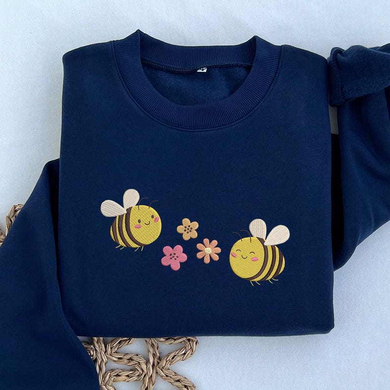 May include: A navy blue sweatshirt with embroidered bees and flowers. The bees are yellow with black stripes and have smiling faces. The flowers are pink and yellow.