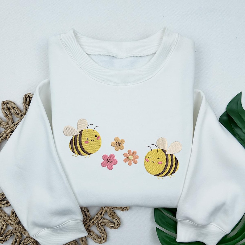 May include: White sweatshirt with embroidered bees and flowers. The bees are yellow and black with smiling faces. The flowers are pink and yellow.