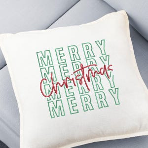 May include: A square, off-white decorative pillow with the words "MERRY" stacked vertically in green block letters. The word "Christmas" is written in red cursive script across the center of the pillow, creating a festive holiday design.