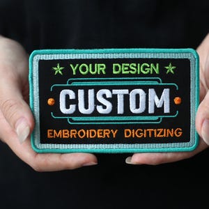 May include: A teal and black embroidered patch with white text that reads "YOUR DESIGN * CUSTOM * EMBROIDERY DIGITIZING".