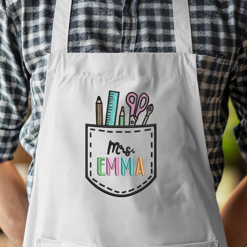 May include: White apron with a pocket design featuring school supplies and the name "Mrs. Emma" in colorful letters. The pocket includes a pencil, ruler, scissors, and a pen.