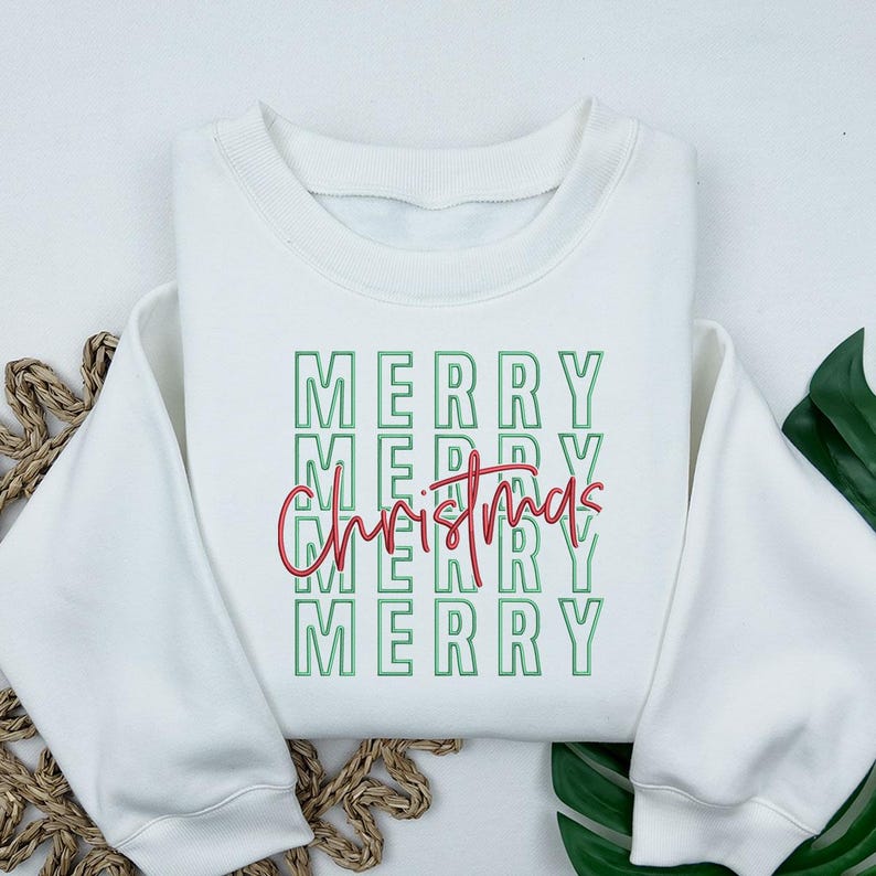 May include: White sweatshirt with the words "MERRY" stacked vertically in green, with "Christmas" in red script overlaid. The sweatshirt has a crew neck and long sleeves, perfect for the holiday season.