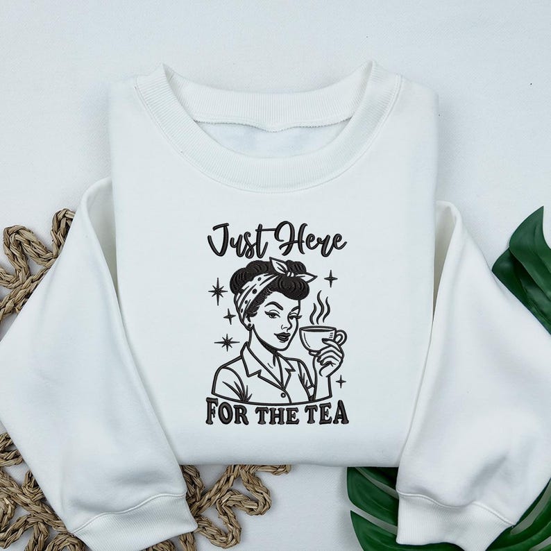 May include: White sweatshirt with a black and white graphic of a woman holding a teacup, wearing a bandana. The text "Just Here For The Tea" is above and below the illustration. The sweatshirt has long sleeves and a crew neck.
