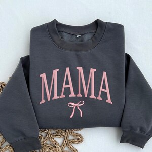 May include: A dark gray sweatshirt with the word "MAMA" in pink lettering and a pink bow underneath.