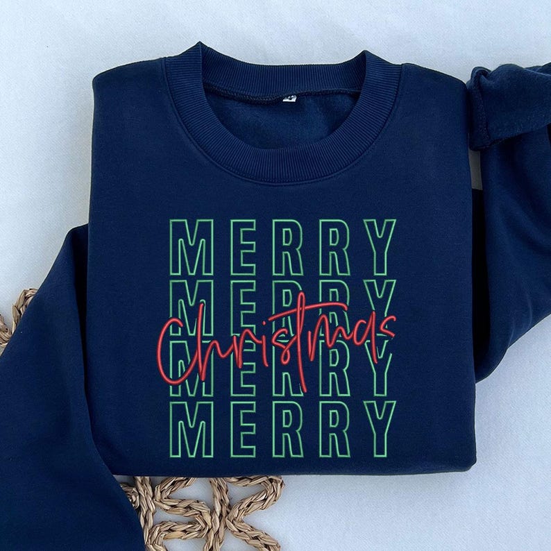 May include: Navy blue sweatshirt with the words "MERRY CHRISTMAS" in green and red. The word "MERRY" is stacked four times in a green outlined font. The word "Christmas" is written in a cursive red font.