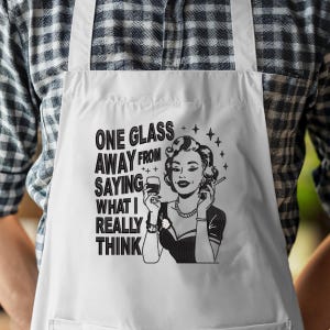 May include: White apron with the text "ONE GLASS AWAY FROM SAYING WHAT I REALLY THINK" and a black and white illustration of a woman holding a glass of wine and a cigarette.