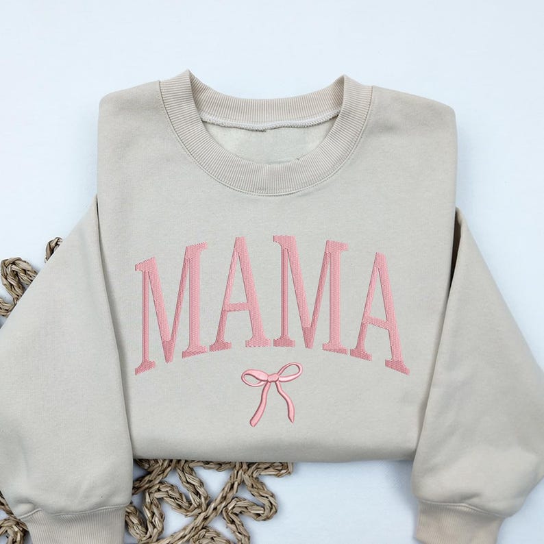 May include: A beige sweatshirt with the word "MAMA" embroidered in pink with a pink bow underneath.