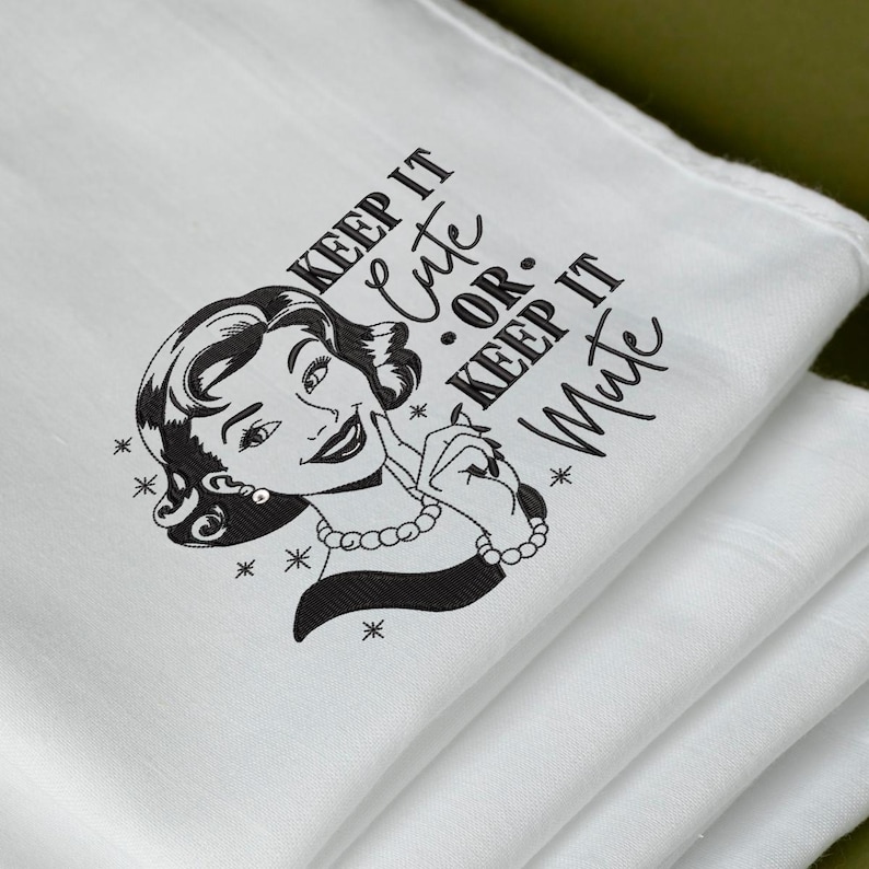 May include: White kitchen towel with a retro illustration of a woman and the text "KEEP IT CUTE OR KEEP IT MUTE" in black. The woman is wearing a pearl necklace and earrings. The towel is folded.