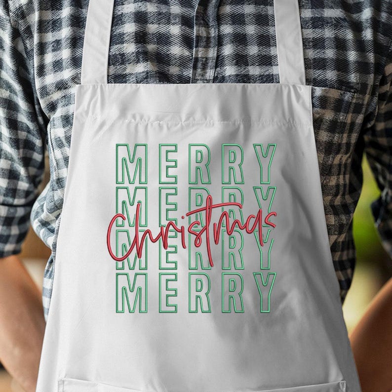 May include: White apron with the words "MERRY CHRISTMAS" in green and red lettering. The word "MERRY" is stacked vertically four times, with "Christmas" in a cursive font in the center. The apron is made of a light-colored fabric.
