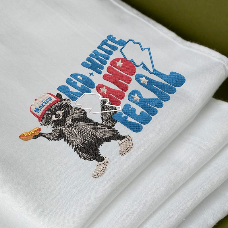 Op de afbeelding: Witte doek met een geborduurd ontwerp met een wasbeer met een hoed met de tekst "Merica" en een hotdog. De tekst "Red, White, and Feral" is geborduurd in rood en blauw.