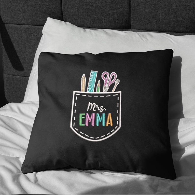May include: Black decorative pillow with a pocket design featuring school supplies and the text "Mrs. Emma" in colorful letters. The pocket design includes a pencil, ruler, scissors, and other school supplies.