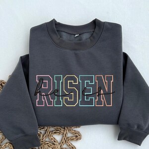May include: A charcoal gray sweatshirt with the words "He is Risen" in rainbow colored letters.