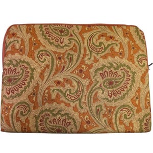 Puede incluir: Una bolsa rectangular con cremallera y estampado de cachemira. El diseño presenta grandes formas de cachemira ornamentadas en tonos naranja, verde y crema. La cremallera y el ribete son de color naranja rojizo.