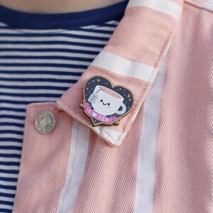 May include: A pink and white striped denim jacket with a wooden pin featuring a cartoon teacup with a tea bag, stars, and a crescent moon. The pin says "I love tea".