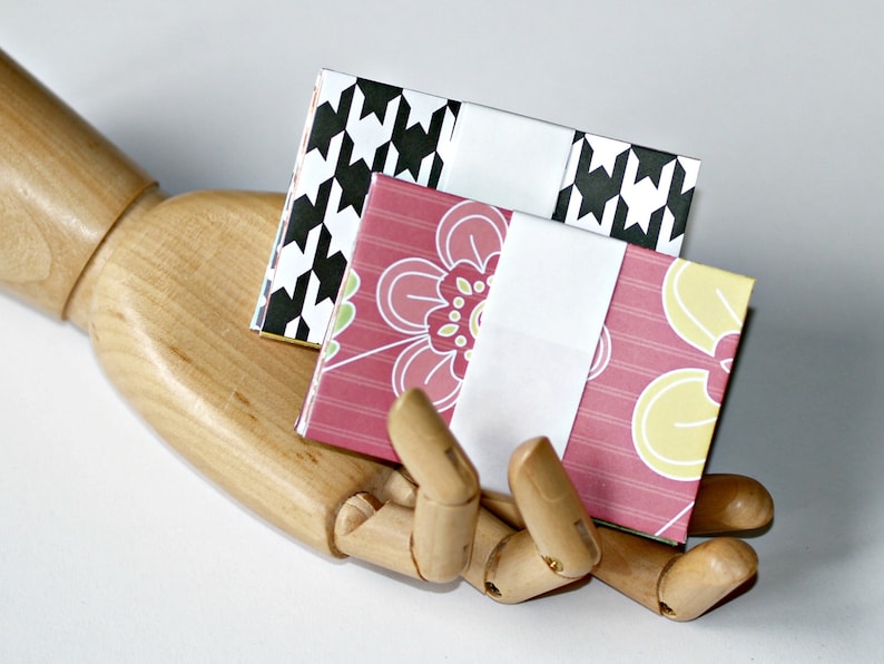 Op de afbeelding: Twee kleine, handgemaakte papieren enveloppen. E&eacute;n envelop is roze met een wit bloemenontwerp en de andere is zwart-wit met een ruitjespatroon.