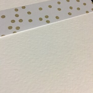 May include: A white card with a gold polka dot patterned strip across the top.