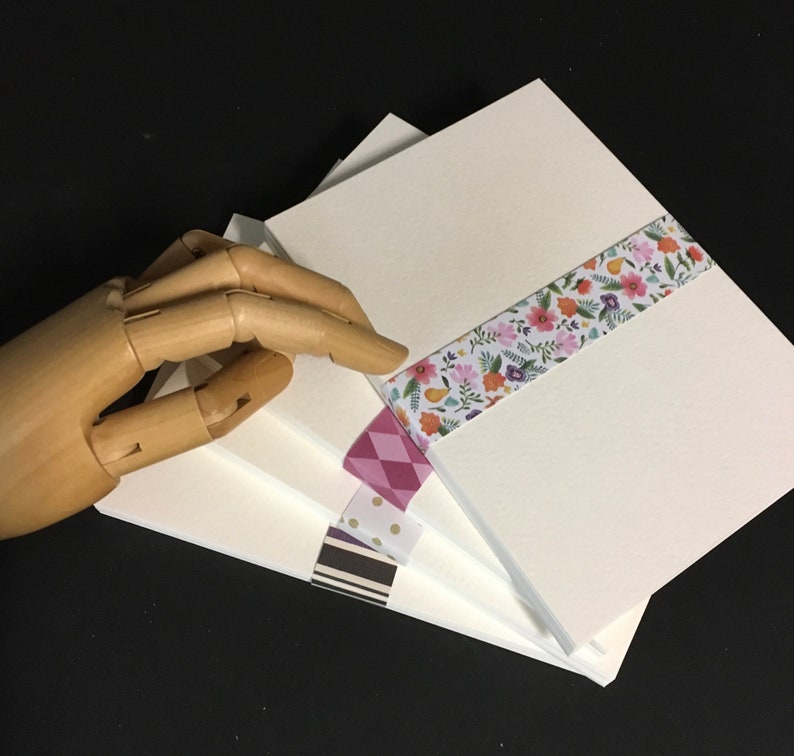 May include: Stack of four white cardstock sheets with decorative washi tape on the top sheet. The tape features a floral pattern with pink, orange, and yellow flowers.