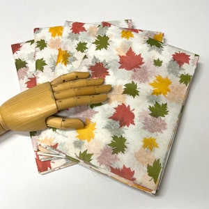 May include: A stack of white tissue paper with a fall leaf pattern in shades of red, orange, yellow, and green. The leaves are printed on the paper and have a watercolor effect.