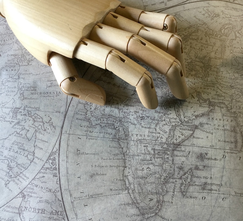 Pu&ograve; includere: Un modello di mano in legno appoggiato su una mappa del mondo vintage. La mappa mostra i continenti di Africa, Asia e Australia. La mano &egrave; in legno marrone chiaro e ha cinque dita.