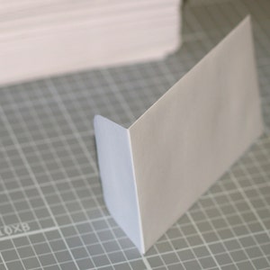 May include: A white envelope with a slightly blue tint on the edges, lying on a gray grid surface.