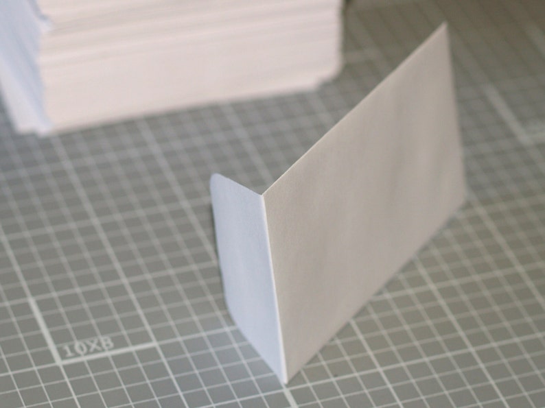 May include: A white envelope with a slightly blue tint on the edges, lying on a gray grid surface.