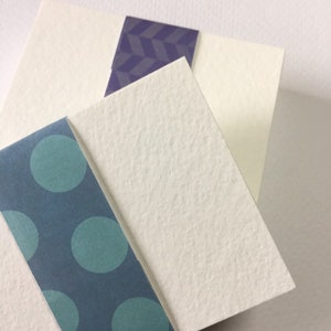 May include: Three white cardstock sheets with different patterned paper borders. The top sheet has a purple geometric pattern, the middle sheet has a blue polka dot pattern, and the bottom sheet has a teal polka dot pattern.