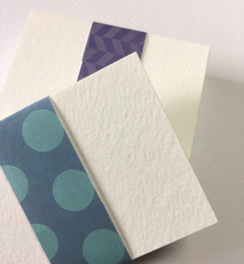 May include: Three white cardstock sheets with different patterned paper borders. The top sheet has a purple geometric pattern, the middle sheet has a blue polka dot pattern, and the bottom sheet has a teal polka dot pattern.