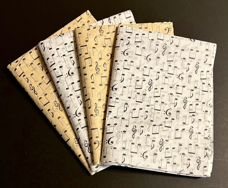 May include: Four sheets of tissue paper with a black musical note pattern. The sheets are in different shades of beige and white.