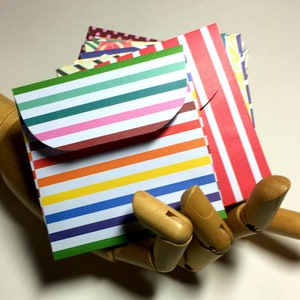 May include: A stack of colorful striped paper envelopes with a flap. The envelopes are folded and ready to be used for sending letters or notes.