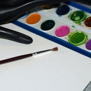 Peut inclure: Une feuille de papier aquarelle blanche avec un pinceau et une palette de peinture aquarelle avec diff&eacute;rentes couleurs de peinture.
