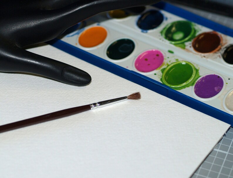 Peut inclure: Une feuille de papier aquarelle blanche avec un pinceau et une palette de peinture aquarelle avec diff&eacute;rentes couleurs de peinture.