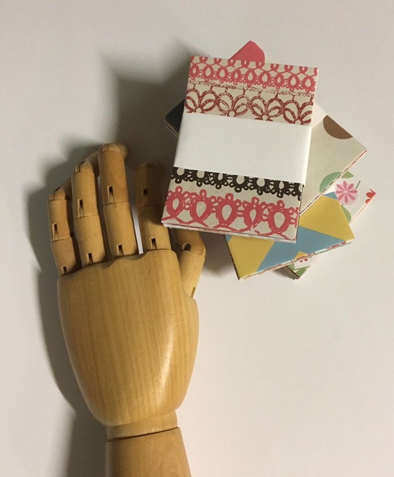 Peut inclure: Un ensemble de quatre petits carnets faits &agrave; la main avec des couvertures aux motifs color&eacute;s. Les couvertures pr&eacute;sentent une vari&eacute;t&eacute; de motifs, notamment des motifs floraux, g&eacute;om&eacute;triques et de dentelle. Les carnets sont reli&eacute;s avec une reliure blanche et ont une &eacute;tiquette blanche vierge sur la couverture avant.