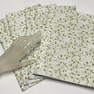 May include: A stack of six white tissue paper sheets with a green leaf pattern. The paper is thin and translucent, and the leaves are a light green color.