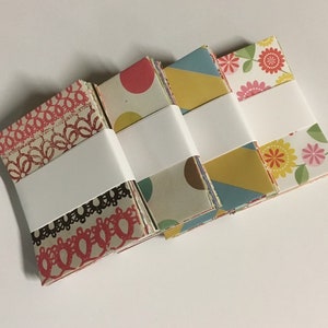 Peut inclure: Quatre piles de papier &agrave; motifs, chaque pile &eacute;tant envelopp&eacute;e de papier blanc. Les motifs comprennent de la dentelle, des pois, des formes g&eacute;om&eacute;triques et des fleurs.