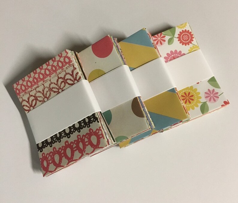 Peut inclure: Quatre piles de papier &agrave; motifs, chaque pile &eacute;tant envelopp&eacute;e de papier blanc. Les motifs comprennent de la dentelle, des pois, des formes g&eacute;om&eacute;triques et des fleurs.