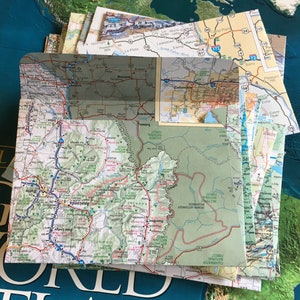 May include: A close-up of a folded map of the western United States, showing the state of Montana. The map is green and brown with blue lines representing roads. The map is folded in half and the top half is visible. The map is labeled with the names of towns and cities, including Anaconda, Butte, Deer Lodge, and Missoula.