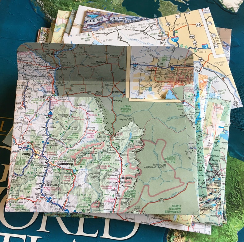 May include: A close-up of a folded map of the western United States, showing the state of Montana. The map is green and brown with blue lines representing roads. The map is folded in half and the top half is visible. The map is labeled with the names of towns and cities, including Anaconda, Butte, Deer Lodge, and Missoula.