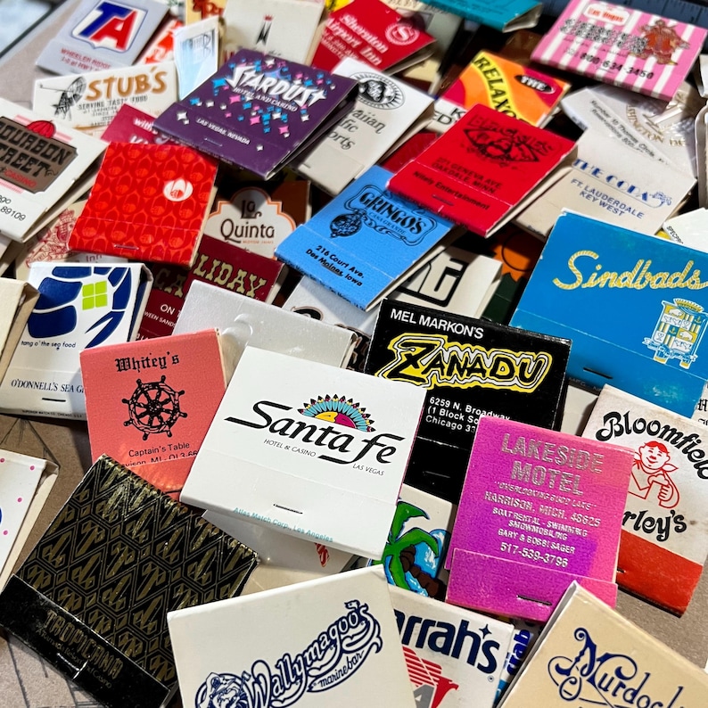 May include: A collection of vintage matchbook covers with various designs and text. The matchbooks feature a variety of businesses and locations, including hotels, restaurants, and motels. Some of the matchbooks have colorful designs, while others are more simple. The matchbooks are a great example of vintage advertising and ephemera.