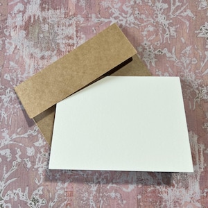 May include: A blank white card with a brown envelope. The envelope is folded over the card.