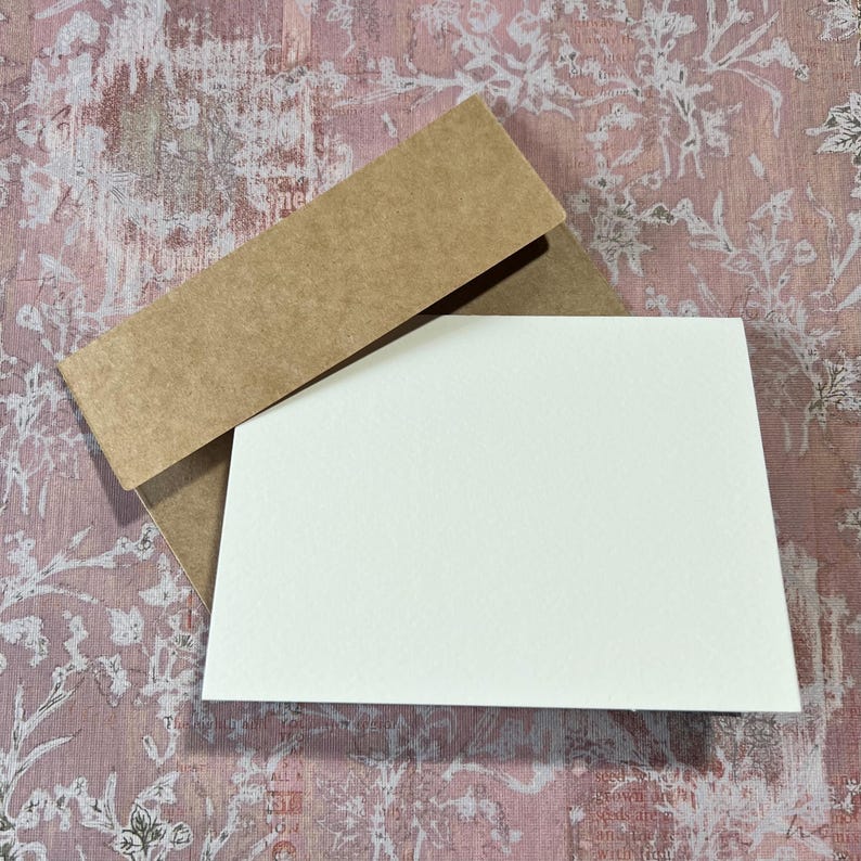 May include: A blank white card with a brown envelope. The envelope is folded over the card.