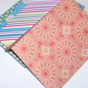May include: A stack of patterned paper with a red and cream design on top. The paper has a delicate lace pattern.